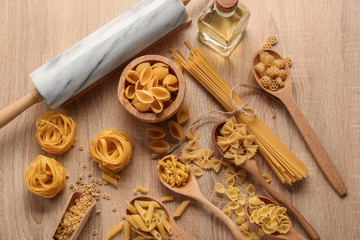 Fototapeta premium Assortment of dry pasta varieties with a marble rolling pin and olive oil on a light wooden table, top view