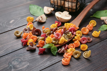 Spoon with colorful raw pasta on dark wooden table
