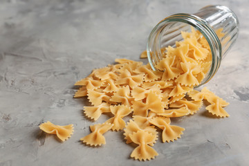 Overturned glass with uncooked farfalle pasta on grey table