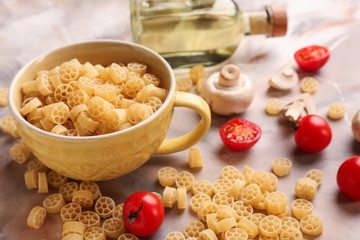 Cup with raw pasta and tomatoes on color table