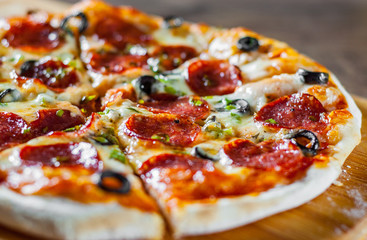 Pizza with Mozzarella cheese, pepperoni, tomato, pepper, olive, salami. Italian pizza on wooden table background