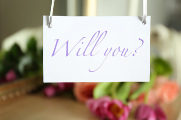 Paper with text WILL YOU? on blurred background. Marriage proposal