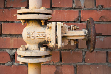 Gas pipes and a valve against a red brick wall. Close-up.