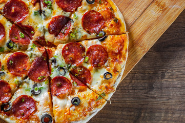 Pizza with Mozzarella cheese, pepperoni, tomato, pepper, olive, salami. Italian pizza on wooden table background