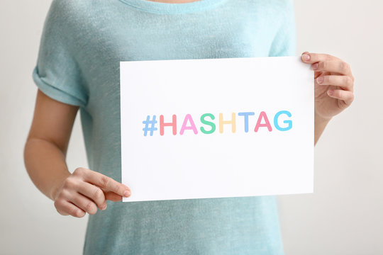 Woman Holding Sheet Of Paper With Hashtag On Light Background