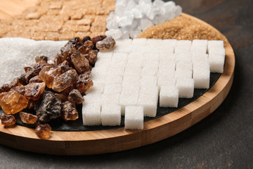 Wooden board with different kinds of sugar on grey background