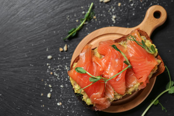 Tasty sandwich with salmon and avocado on dark table
