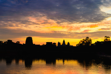 Fototapeta na wymiar Angkor Wat dramatic sky at dawn main facade silhouette reflection on water pond. World famous temple in Cambodia.