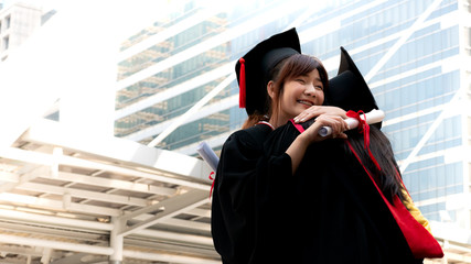 Two girls in black gowns and hold diploma certificate sitting and smiling with happy graduated.