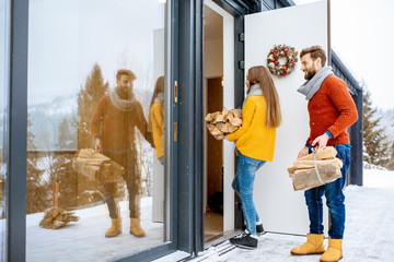 Young lovely couple dressed in colorful sweaters entering their modern home with firewoods in the mountains during the winter