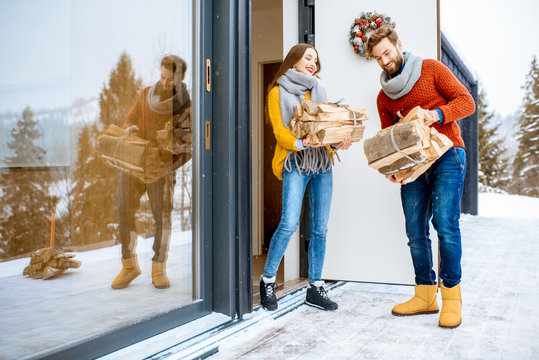 Young Lovely Couple Dressed In Colorful Sweaters Entering Their Modern Home With Firewoods In The Mountains During The Winter