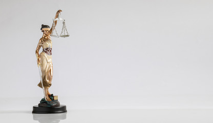 A figure of goddess of justice with scales in her hand is standing on the flat surface at the white background.