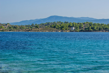 tropic Mediterranean sea beach with vivid blue water surface and small waves with view on opposite forest waterfront coast shoreline