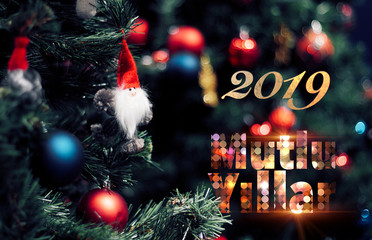 Closeup of red bauble hanging from a decorated pine tree with 2019 text. Mutlu yıllar means Happy new year