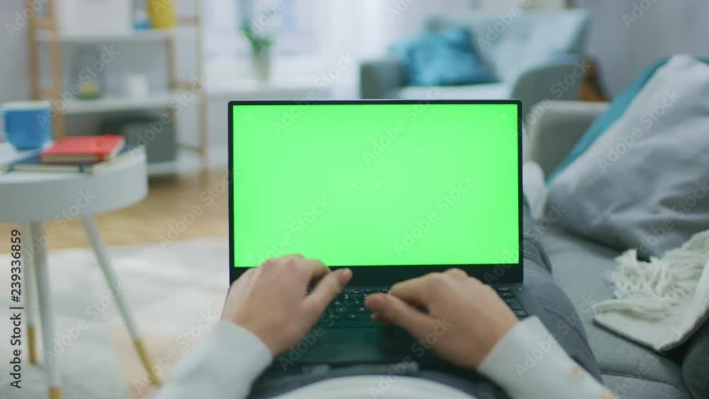 Poster woman at home laying on a couch using laptop computer with green mock-up screen. girl typing on comp