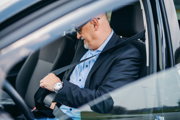 Bearded senior adult businessman fastening seat belt in his car.
