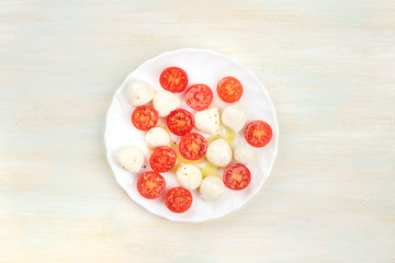 A plate of Italian Caprese salad with Mozzarella cheese and cherry tomatoes, shot from the top on a light background with copy space