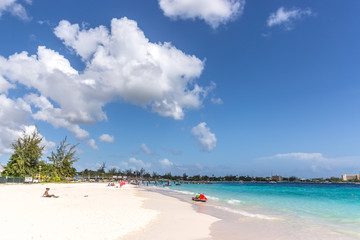 Dover Beach, Barbados - Mar 5th 2018 - Tourists sitting in the white sand with a red jetsky in front of her in a clear water beach in Barbados