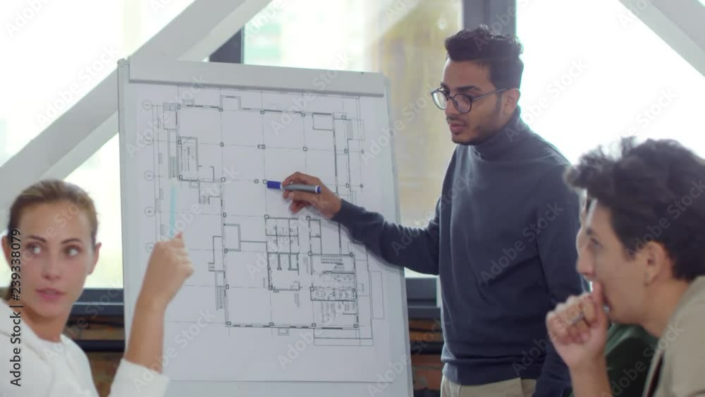 Aufkleber young middle eastern man in eyeglasses explaining architectural project on flipchart to colleagues w