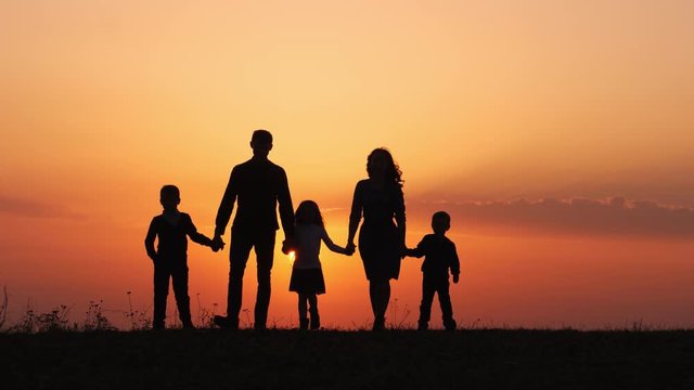 Silhouettes of happy family walking together in the meadow during sunset