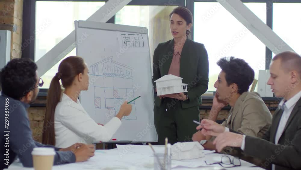 Poster young beautiful businesswoman explaining drawing on flipchart and discussing model of residential bu