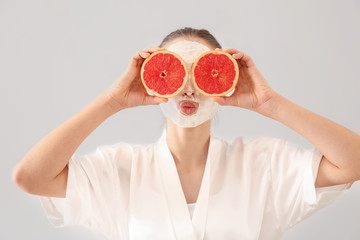 Beautiful young woman with facial mask and grapefruit on light background