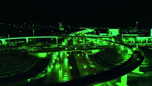 4K. Aerial view of highway road interchange with busy urban traffic speeding on the road at night. Junction network of transportation. Video is tinted green. Timelapse