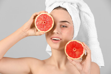 Beautiful young woman with under-eye patches and grapefruit on light background