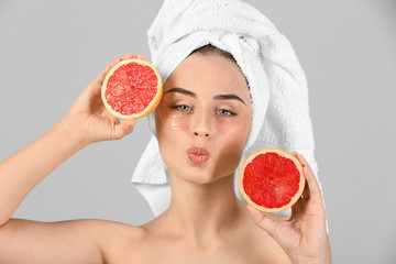 Beautiful young woman with under-eye patches and grapefruit on light background