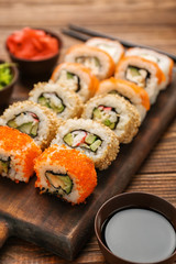 Board with tasty sushi rolls on wooden table