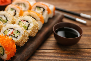 Board with tasty sushi rolls on wooden table