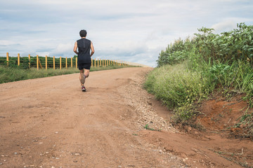 Obraz premium Young man running in the morning. Healthy lifestyle concept. Runner running on road. Young man running on a rural road during sunset.