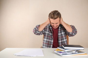 Stressed young man at table on light background