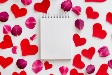 Notebook on the red felt hearts and pink rose petals background. St. Valentine's Day, Romance concept. Top view, flat lay, copy space, mock up
