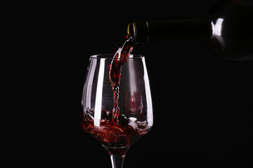 Fototapeta na wymiar Pouring of red wine from bottle into glass on dark background