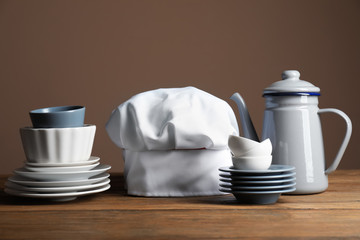 Chef's hat with  kitchenware on table against color background