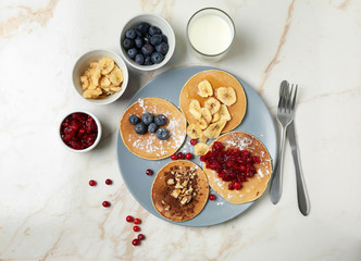 Tasty pancakes with banana slices, berries and glass of milk on light table