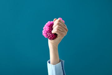 Female hand squeezing stress ball on color background