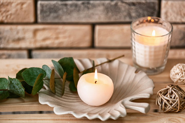 Beautiful burning candles on shelf near brick wall
