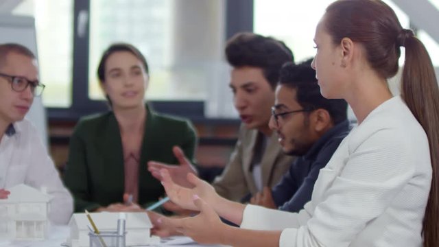 Beautiful caucasian woman discussing architectural project with team of diverse colleagues and then looking at camera and smiling