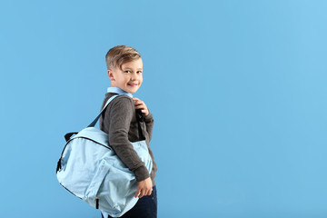 Cute little schoolboy with backpack on color background