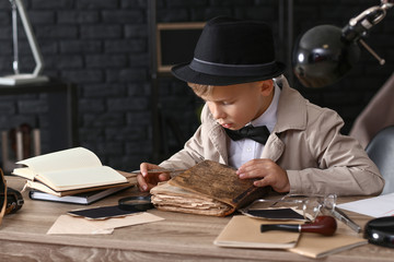 Cute little detective reading old book indoors