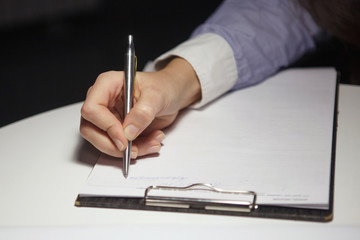 On the table in the night office, a female hand holds a pen on the tablet.