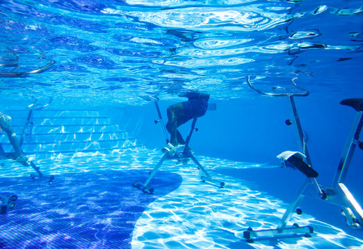 Touristen doing aqua aerobics on exercise bikes in swimming pool tropical hotel