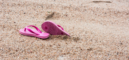 Wide photo of a pair of Red slippers left on top of the brown sand in a beach resort during summer...