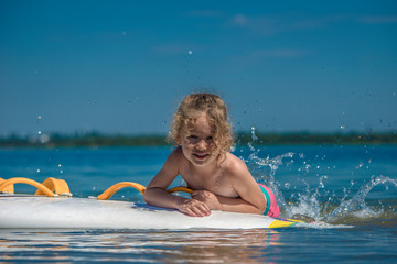 Little cute happy girl with curly hair is lying on the boat in beautiful blue water making spray feet.