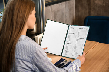 Fototapeta premium Young woman looking through menu in restaurant