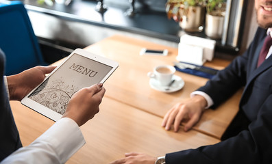 Young waitress with menu on tablet PC screen in restaurant