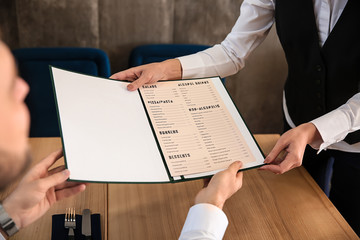 Young waitress showing man a menu in restaurant - obrazy, fototapety, plakaty