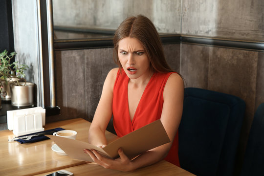 Shocked young woman looking through menu in restaurant